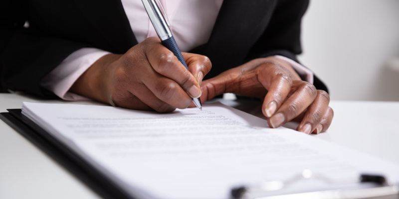 A close-up shot of a businesswoman signing documents at her desk illustrates business compliance with regulations.