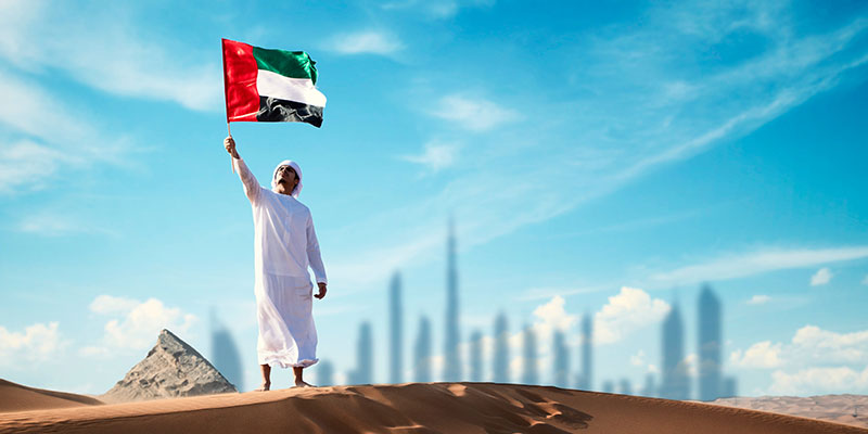 An Arab man holding the UAE flag in the desert illustrates the impact of economic substance regulations in the UAE.