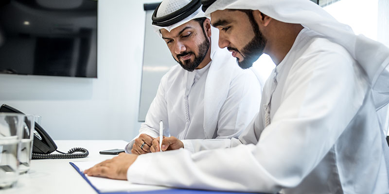 Team of Arab businessmen filling out forms for opening a business bank account in the UAE.