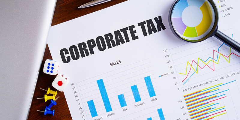 "Corporate Tax" text on paper sheet with magnifying glass on business data chart.
